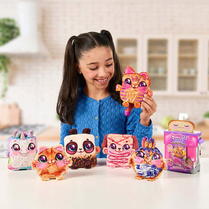 Child holding a cute Cookeez Makery Toasties surprise plush toy with other plushies displayed in a kitchen setting.